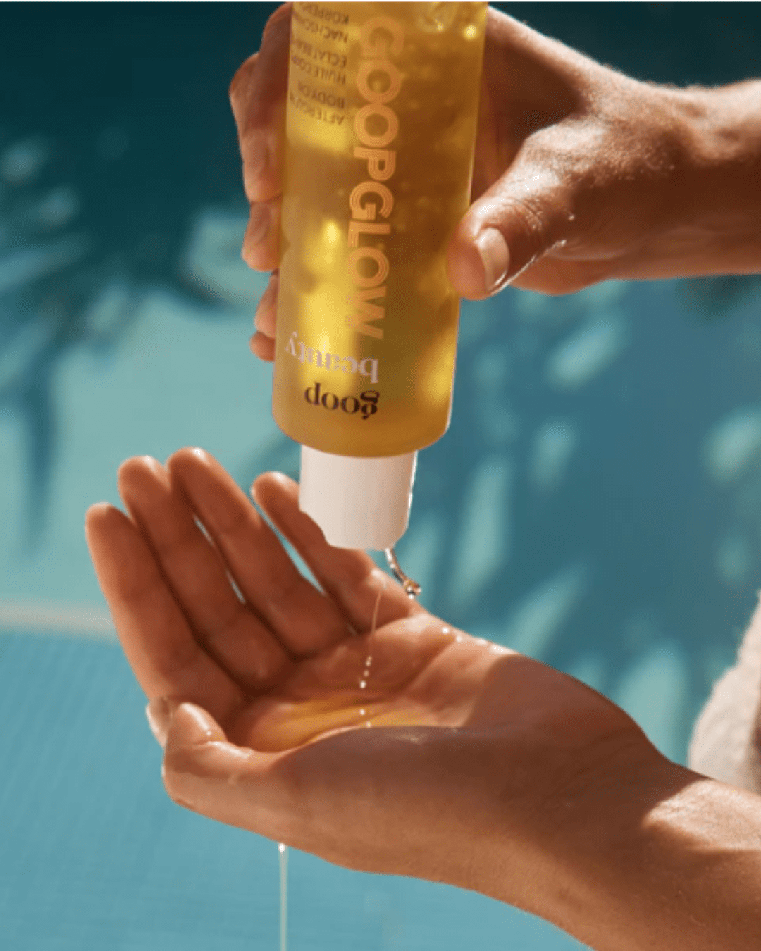 Goop Afterglow Body Oil being poured into a woman's hand. The background is blue with the shadow of a plant. Part of the fall self-care & beauty guide.