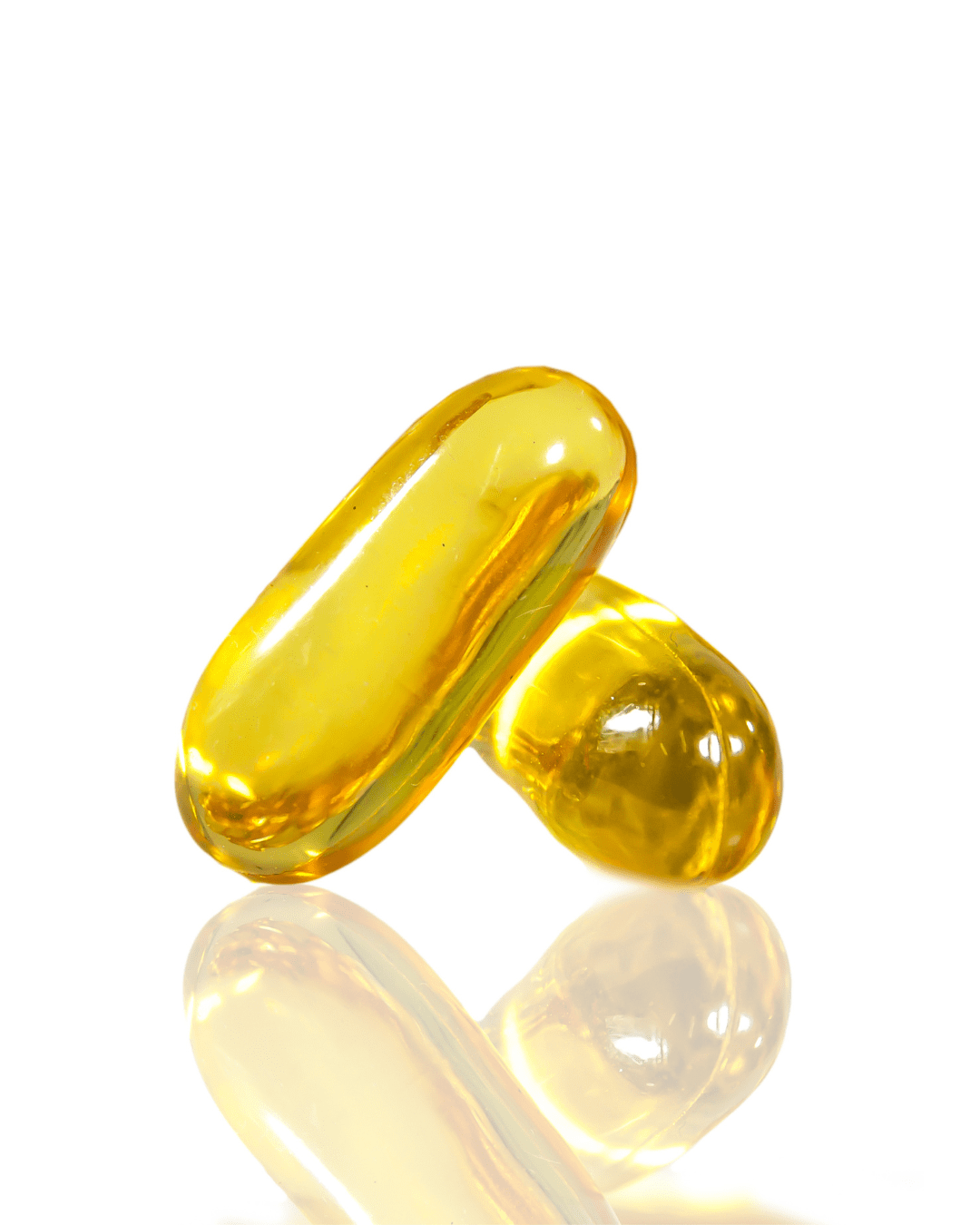 Stacked yellow vitamin capsules representing Omega 3, 6, and 9, key ingredients in the PRAI Beauty Necks-Generation Future Proof Night Cream, on a mirrored reflective surface with a white background.