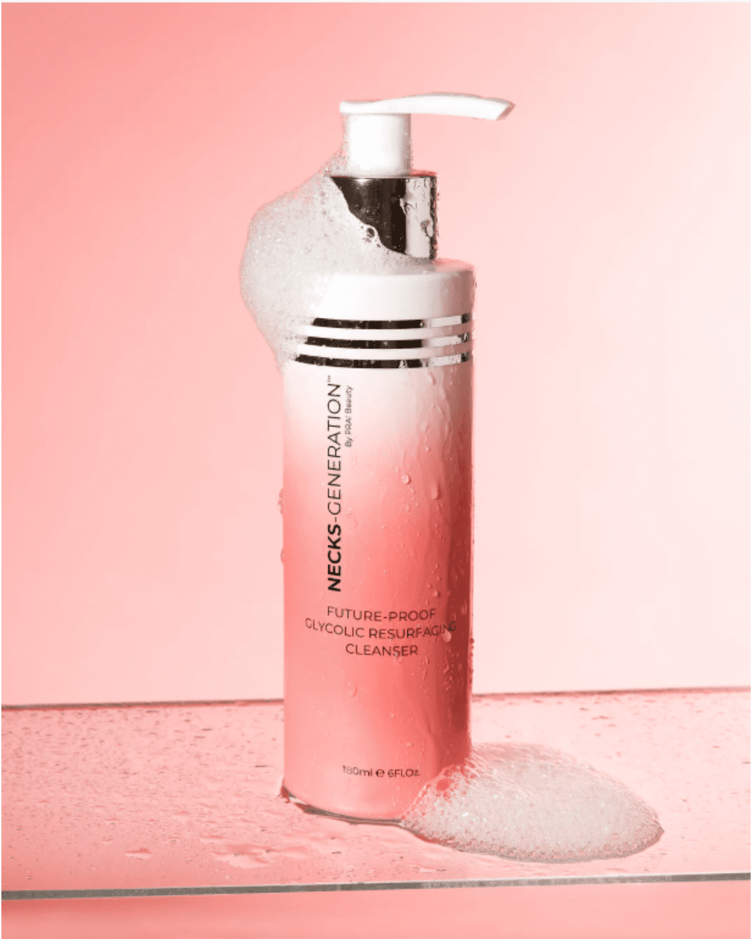 PRAI Beauty Necks Generation Glycolic Cleanser on a pink gradient background with glass surface and water splashes, showing the cleanser on top of the bottle.