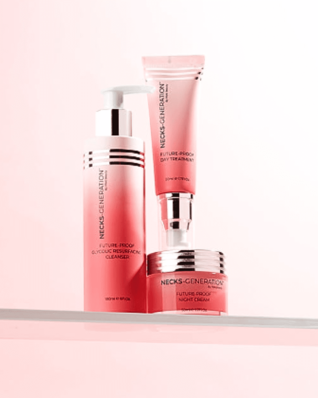 PRAI Beauty Necks Generation Glycolic Cleanser with Necks Generation Futureproof Night Cream and Day Treatment stacked on top of the night cream, on a white shelf against a pink-to-white gradient background.