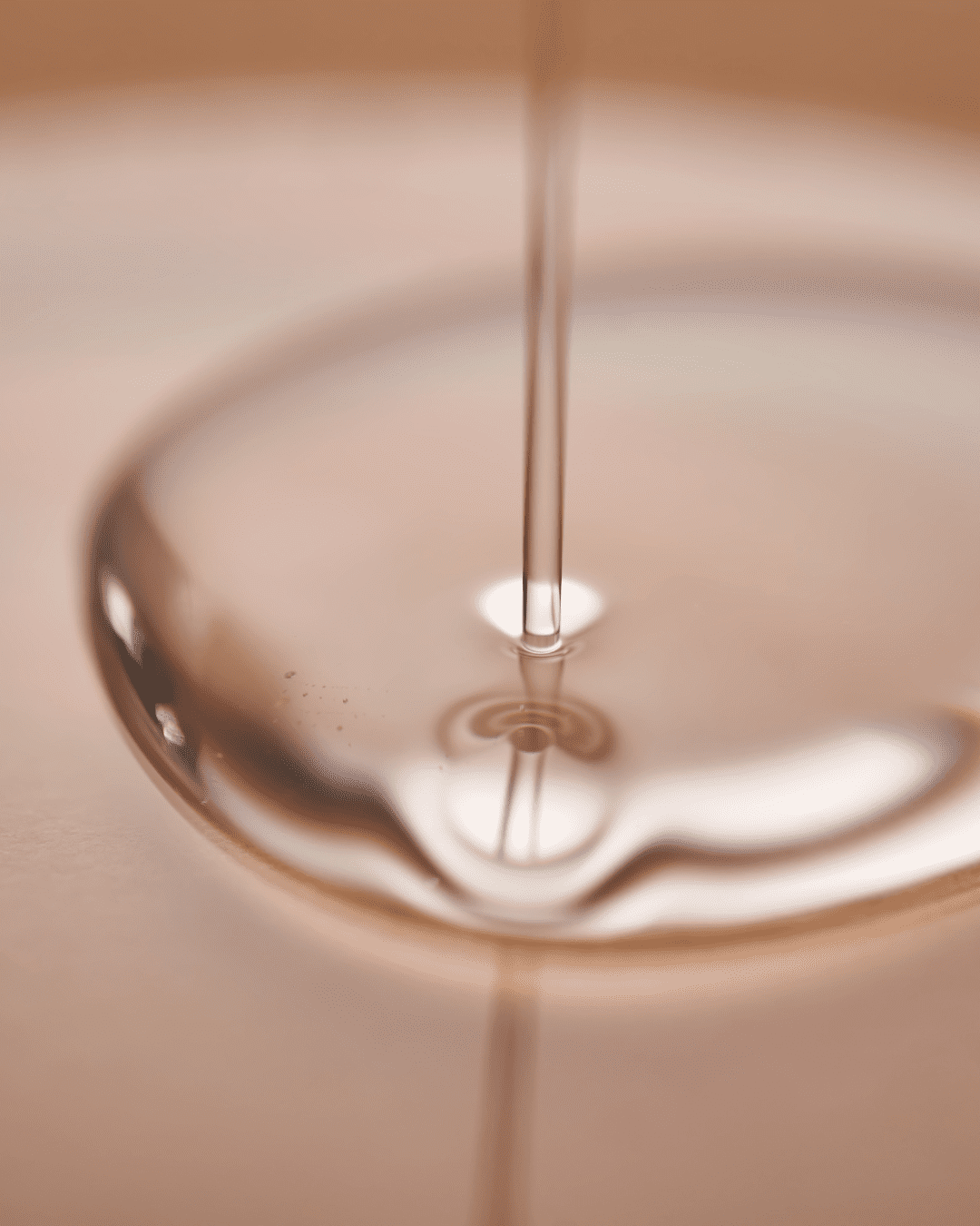 Clear, watery serum being poured onto a surface, representing Squalene, a key ingredient in the PRAI Beauty Necks-Generation Future Proof Night Cream. Part of the fall self-care & beauty guide.
