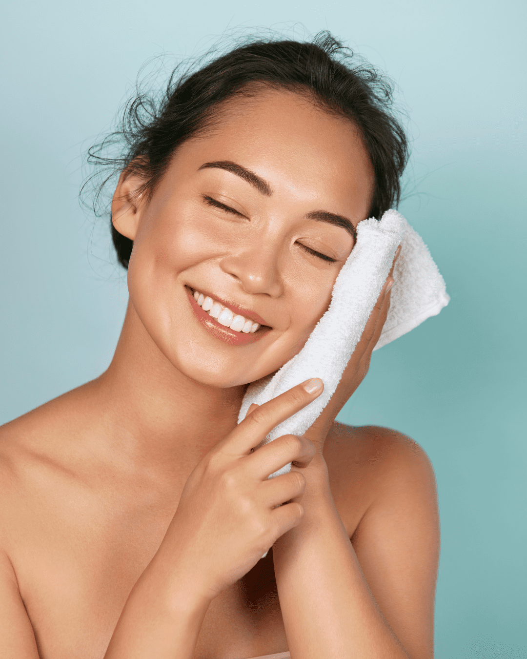 A young woman with brown hair dries her face with a washcloth against a teal background, shown in a step commonly included in honey skincare routines.