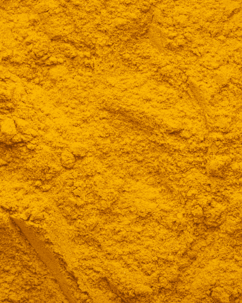 Ground Turmeric powder displayed on a flat surface, emphasizing its vibrant color and use in holistic skincare rituals. An ingredient that can be found in Ayurvedic skincare.