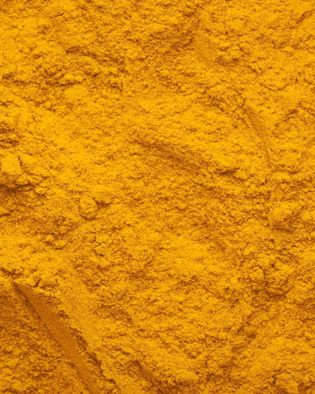 Ground Turmeric powder displayed on a flat surface, emphasizing its vibrant color and use in holistic skincare rituals. An ingredient that can be found in Ayurvedic skincare.