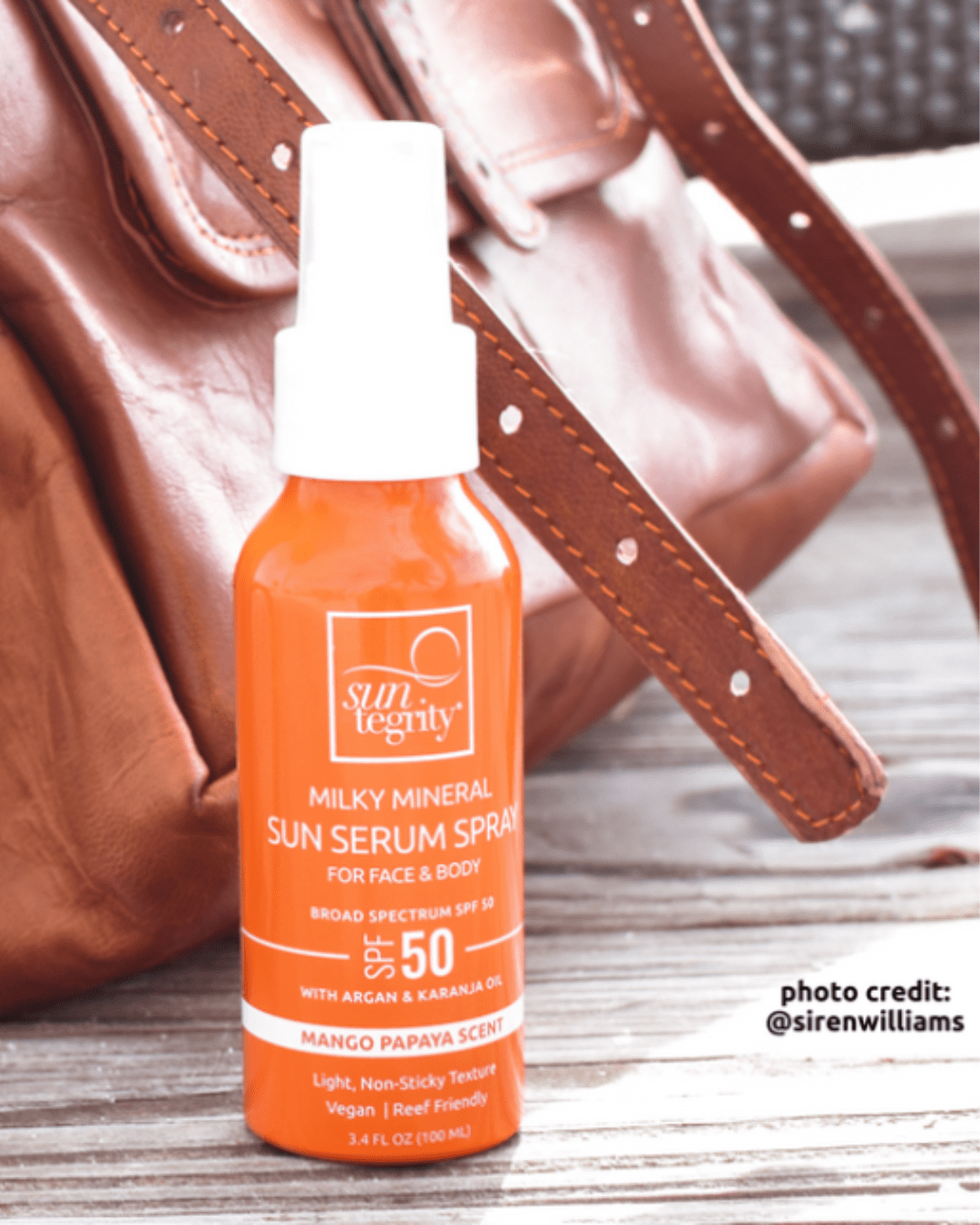 Suntegrity Milky Mineral Sun Serum Spray Broad Spectrum SPF 50 placed next to a purse on a wooden table.