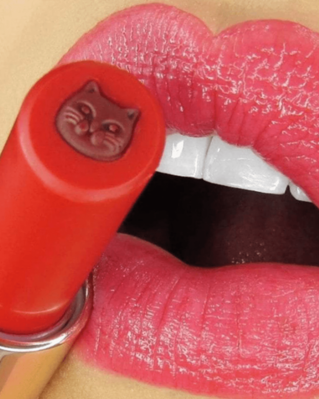 Close-up of lips wearing Winky Lux Purrfect Pout Lipstick shade Furever beside the lipstick tube, showcasing the vibrant pink-red beauty finish.