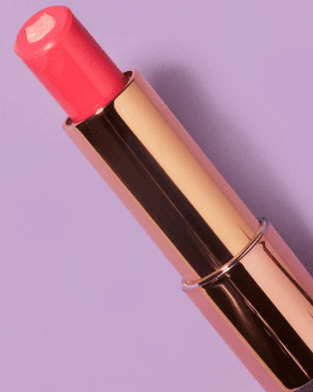 Angled view of Winky Lux Purrfect Pout Lipstick shade Purrincess on a purple background, featuring the pink kitty design and gold-plated case, emphasizing the whimsical beauty aesthetic.