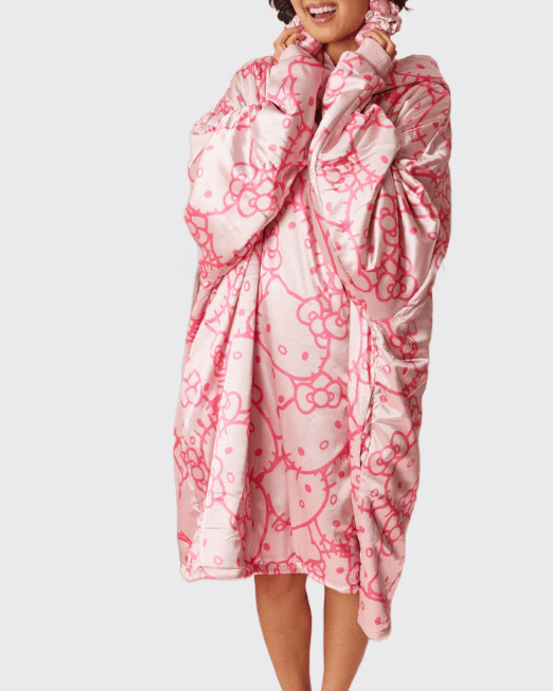 Girl standing against a gray background wearing the Kitsch x Hello Kitty Satin Glazey in light pink with overlapping darker pink Hello Kitty heads, styled with a satin heatless curler in her hair.