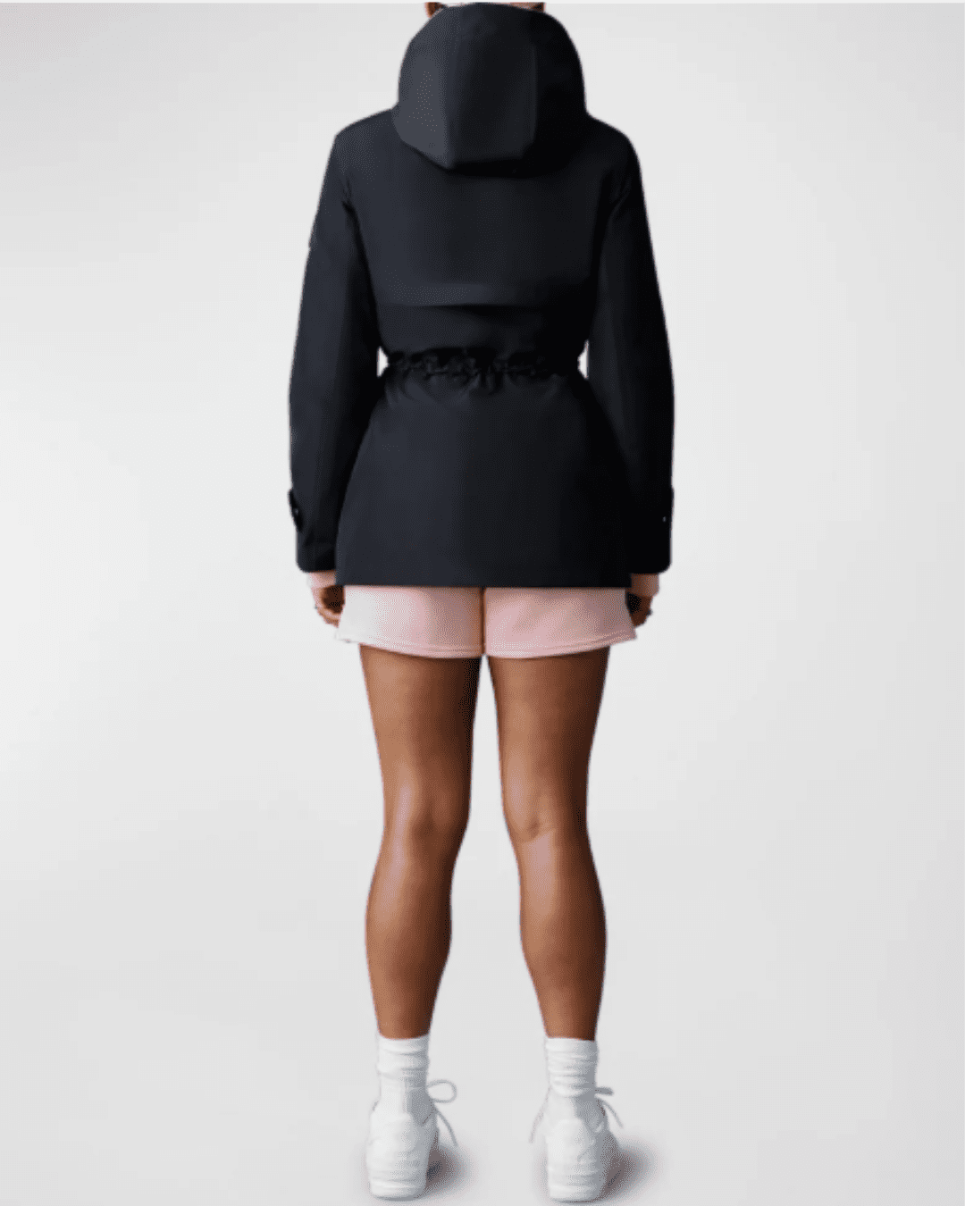 Black woman wearing Mackage Melany Hooded Raincoat, back view, hood up, paired with pink shorts and white shoes, showing full coverage.