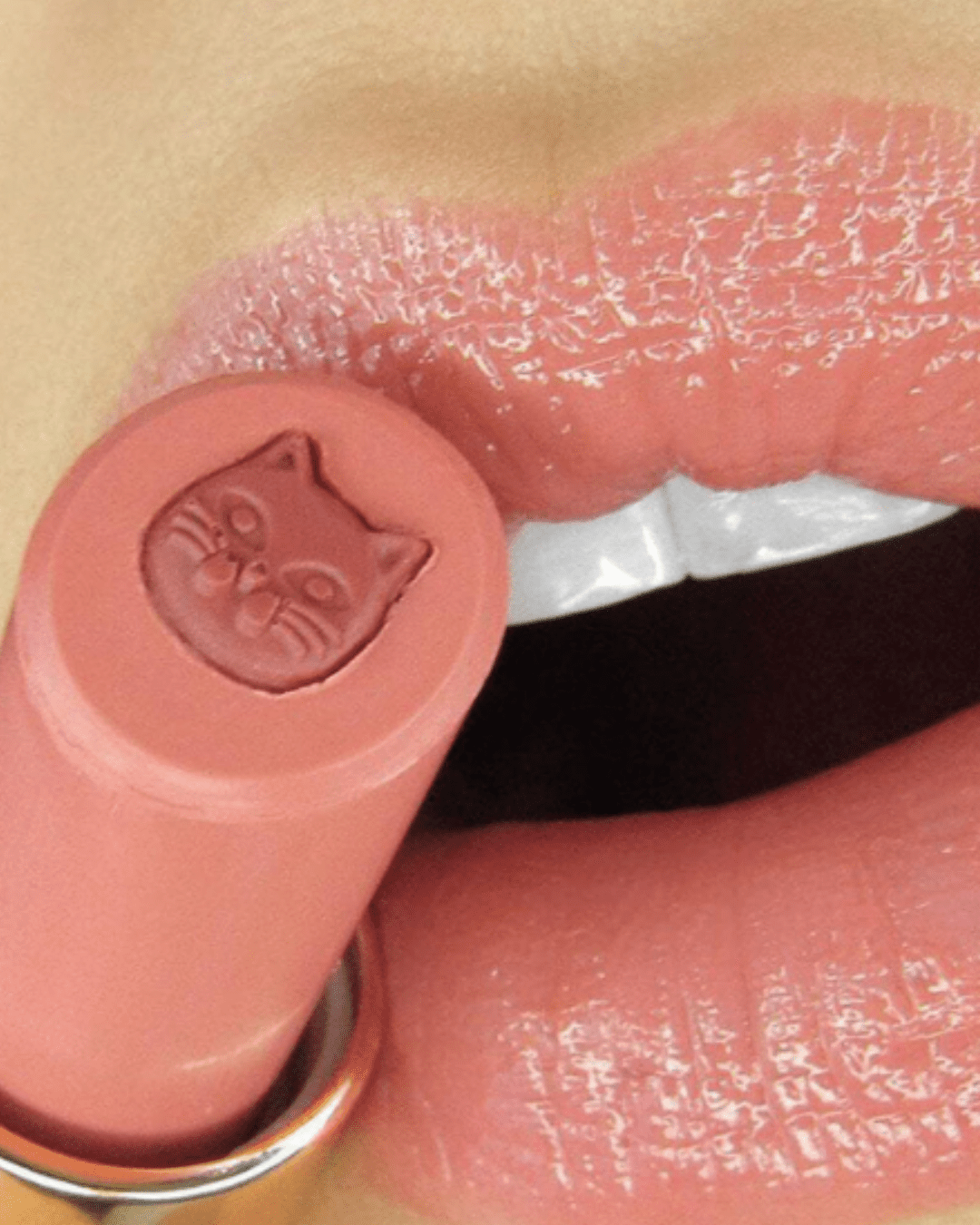 Close-up of lips wearing Winky Lux Purrfect Pout Lipstick shade Pawsh next to the product, showing the kitty design in the lipstick and the rich beauty color payoff.