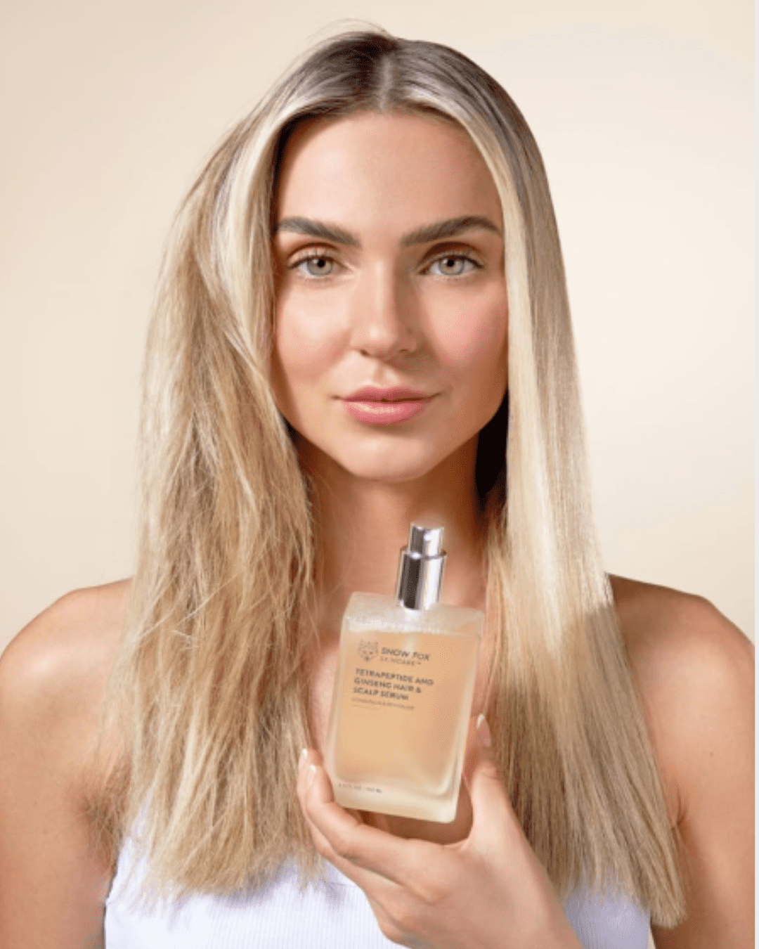 Blonde woman holding SNOW FOX Tetrapeptide and Ginseng Hair and Scalp Serum, left side of hair treated with serum, right side untreated, showing before-and-after effect.