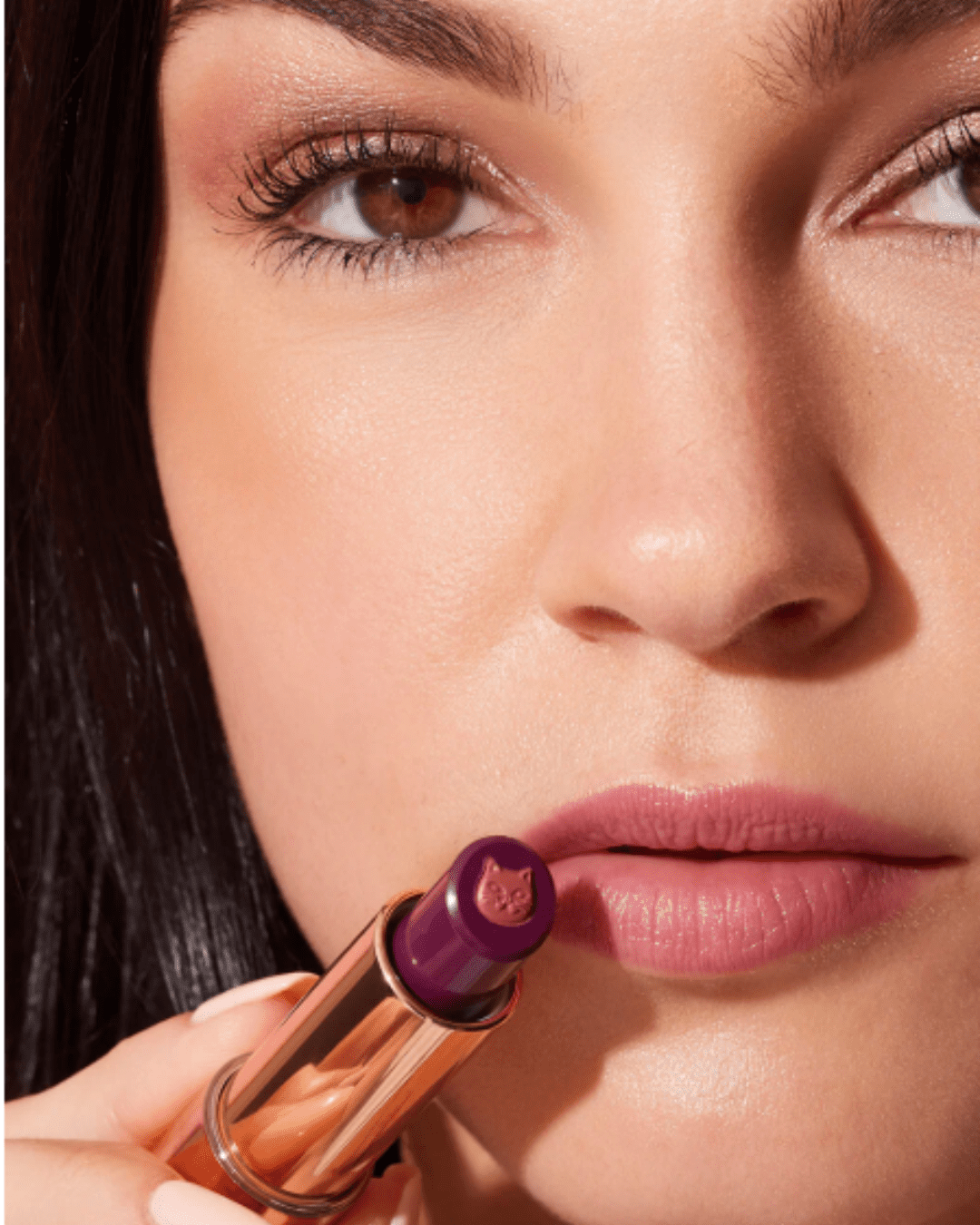 Light-complexion woman with brown hair and brown eyes wearing Winky Lux Purrfect Pout Lipstick shade Frisky, holding the lipstick to her lips, showcasing the playful beauty design.