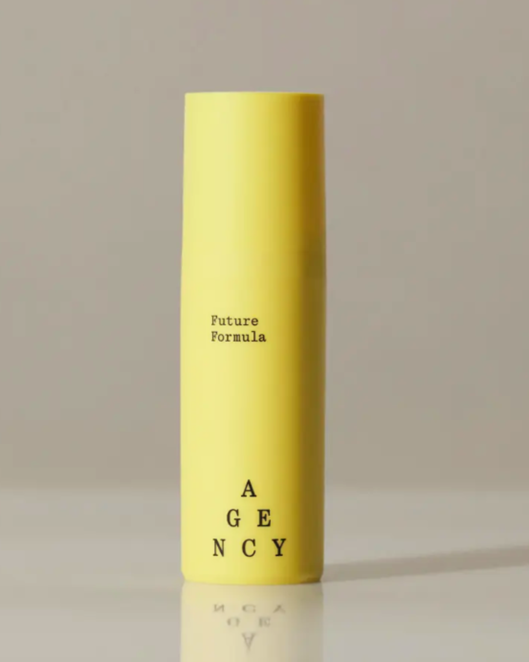 Agency Skincare Future Formula anti-aging moisturizer in a yellow bottle on a reflective white surface with a white background, with "Future Formula" in typewriter text and the Agency logo in a pyramid design.