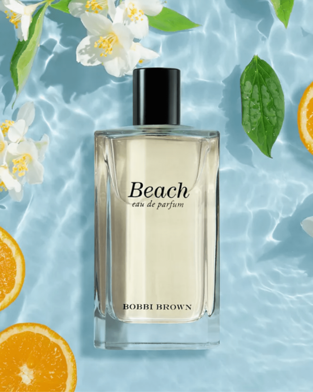 Beach by Bobbi Brown perfume bottle on reflective blue water with orange slices and jasmine leaves-tropical beach perfumes.