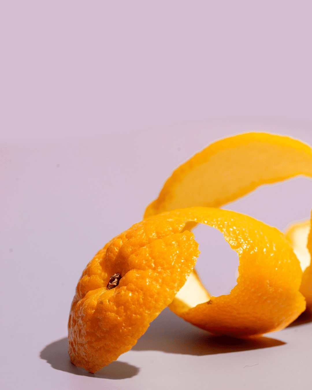 Orange rind spiraled on a lavender background, highlighting citrus fruit extracts featured in FarmHouse Fresh Illumination Fruit Professional Strength Peel.
