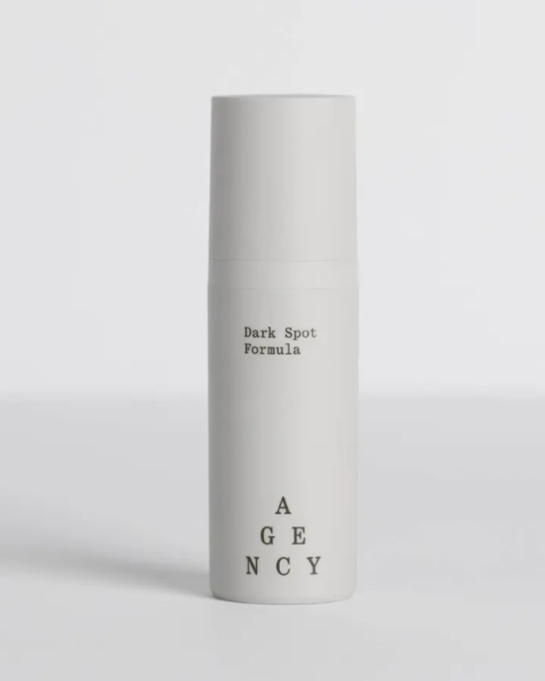 Agency Skincare Dark Spot Formula anti-aging moisturizer in a gray bottle on a gray flat surface with a gray background, showcasing the product design and packaging.