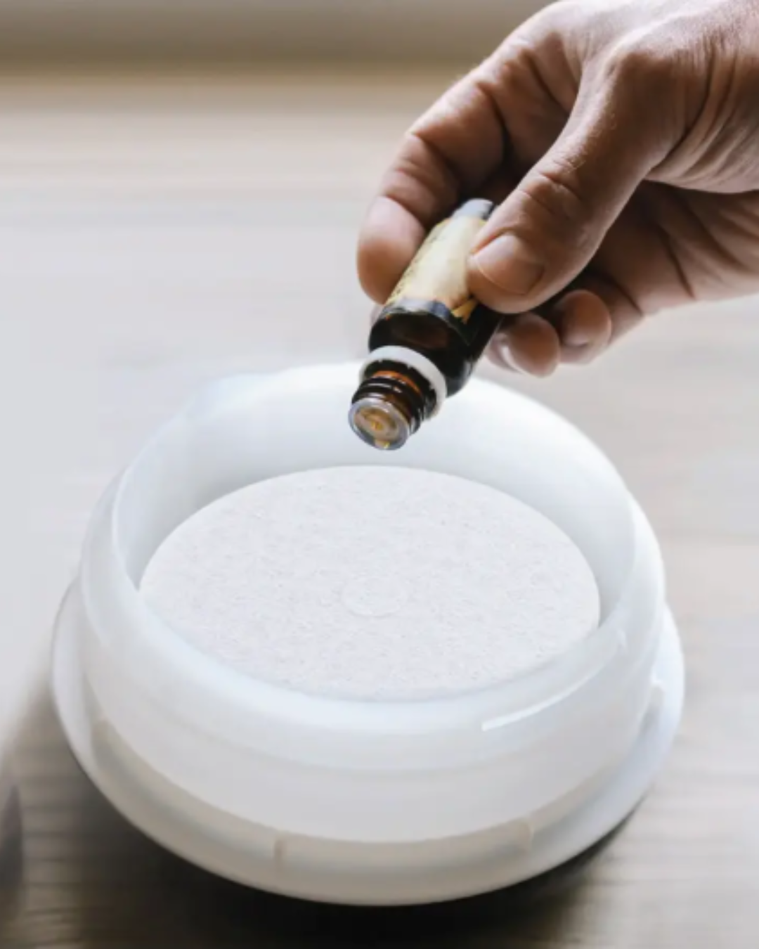 Hand adding essential oil to the Sharper Image Spa Studio Towel Warmer's essential oil removable cap with a cotton round in it, creating a fragrant experience for a soothing self-love practice.