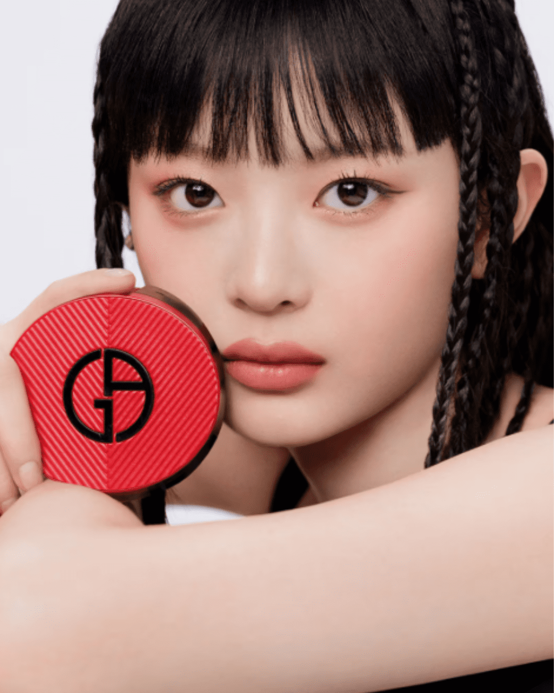 Hanni from NewJeans holding Giorgio Armani To Go Cushion Refill to her cheek with arms crossed, showing product and packaging.