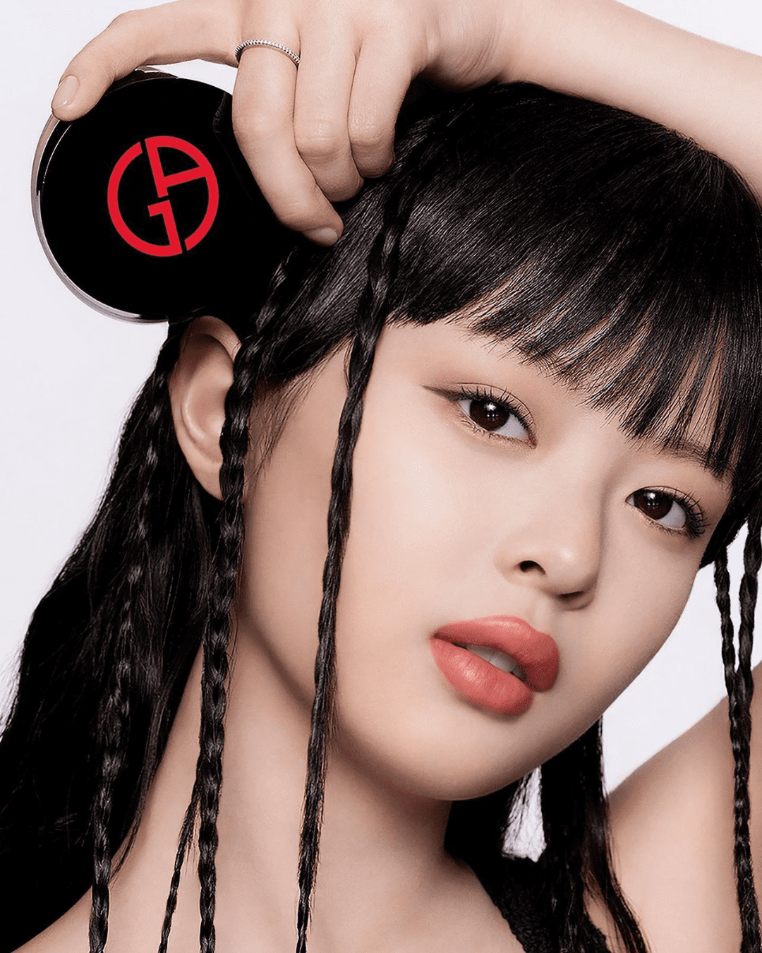 Hanii from NewJeans posing with Giorgio Armani Power Fabric Compact Cream Foundation Balm, arm raised, and hair has some braids.