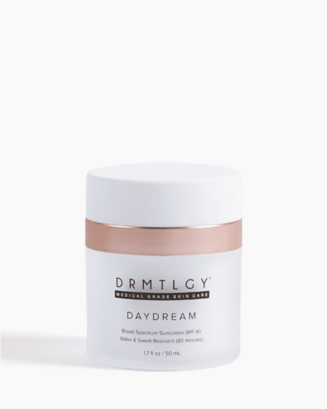DRMTLGY Daydream SPF 40 in a circular press bottle with a rose gold band and white lid, on a flat white surface with soft shadows and a white background, showing the product packaging and dispenser design.