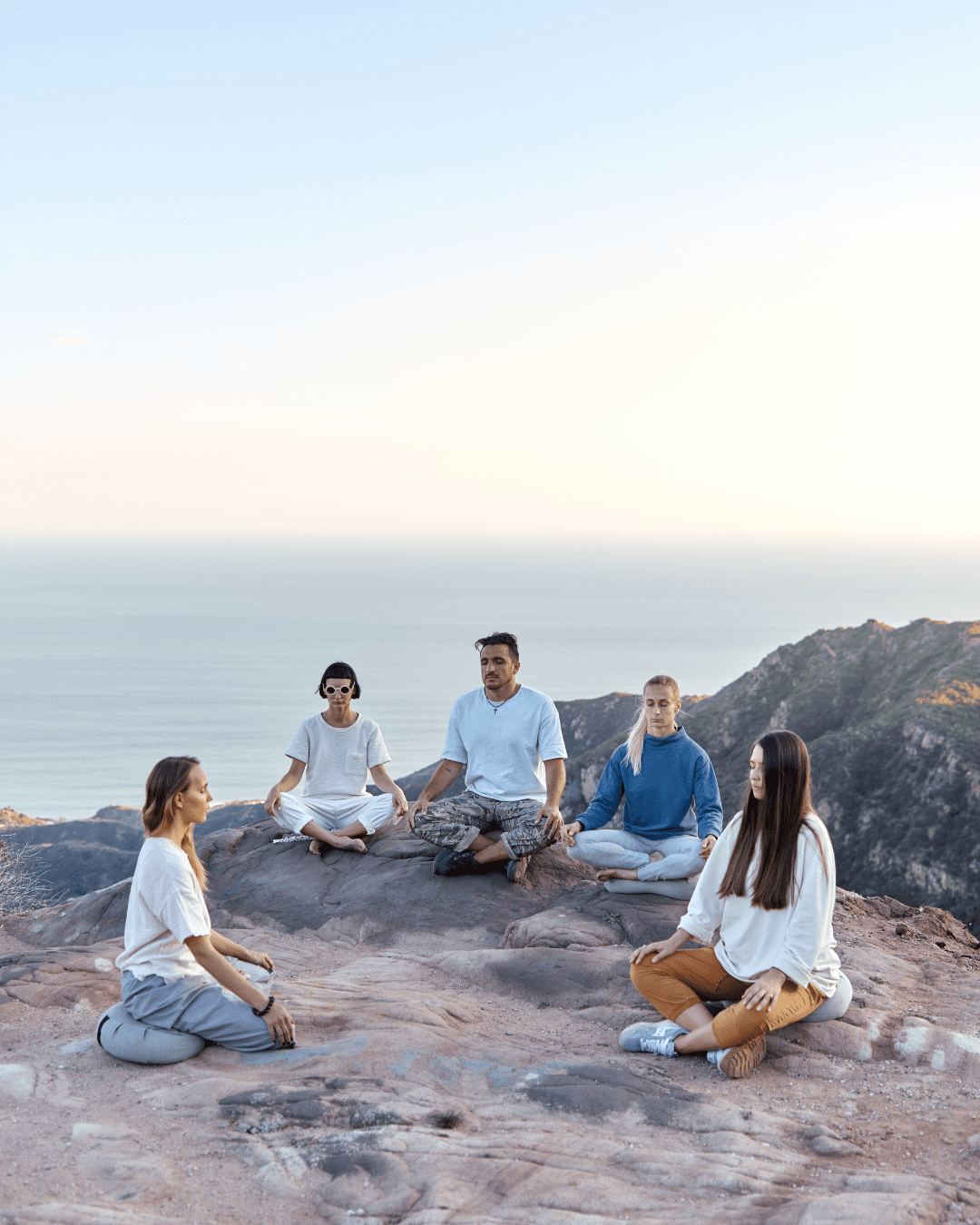Group of young people sitting on the beach in a circle meditating, representing people wearing acne safe sunscreen.
