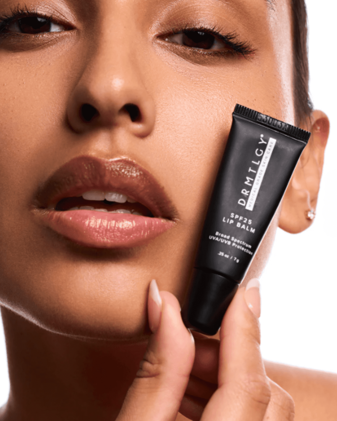 Close-up on an Indian woman pressing DRMTLGY SPF 25 Lip Balm against her cheek, highlighting her lips and demonstrating lip protection and hydration.