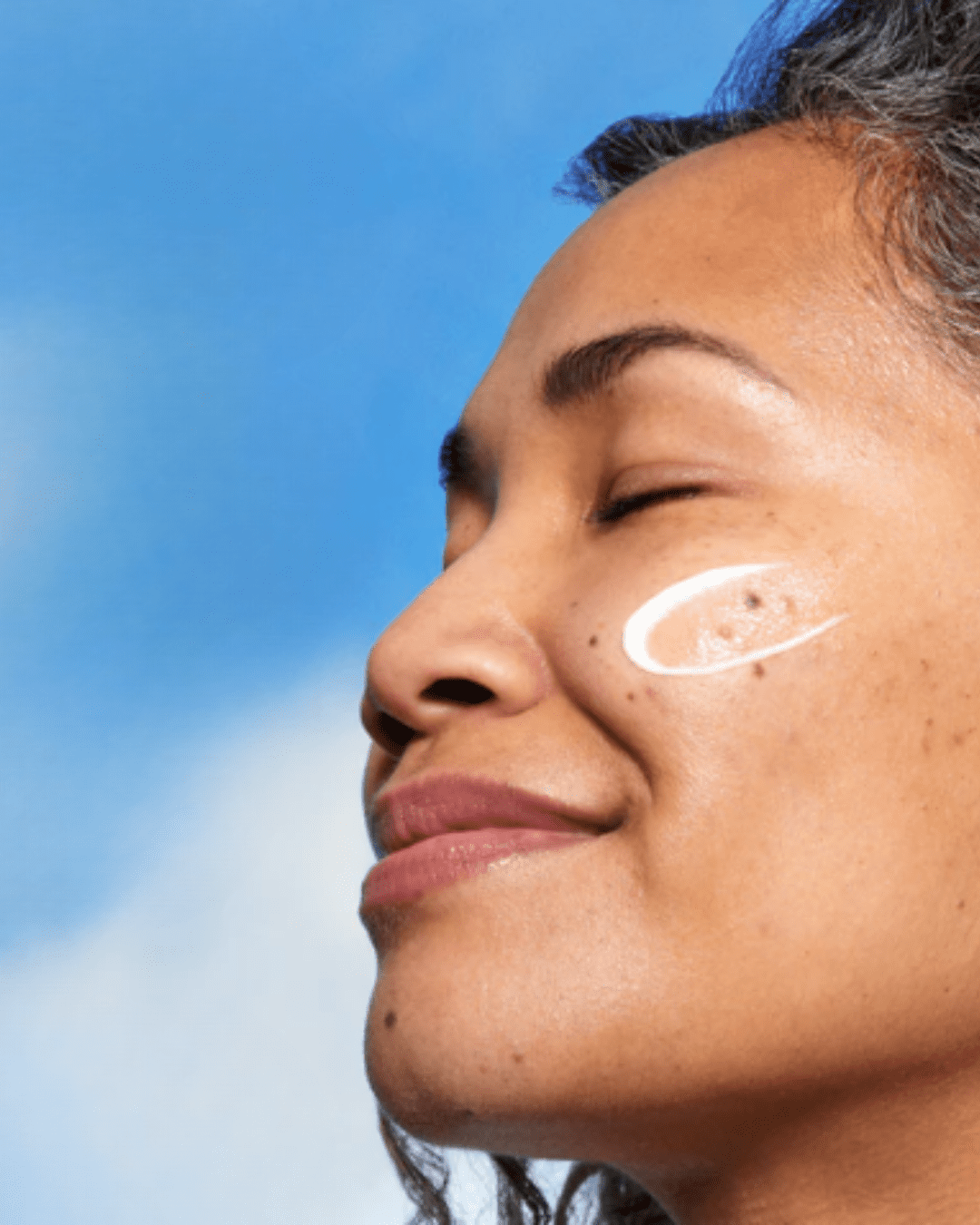 Mexican, or brown-skinned woman with eyes closed, face at an angle, with a swatch of Glow Recipe Watermelon Glow Dew Shield SPF 30 on her cheek, suitable for acne.