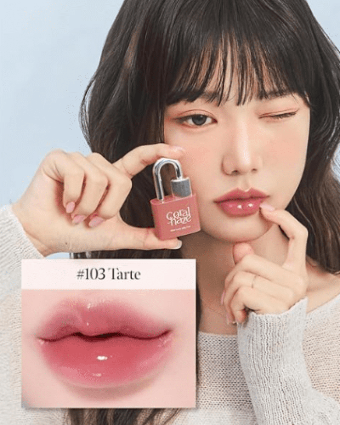 Model wearing Coral Haze lip tint in shade 103 Tart, holding the lock-shaped product to her cheek and winking, with an inset close-up of glossy pink lips, demonstrating a joyful self-love practice.