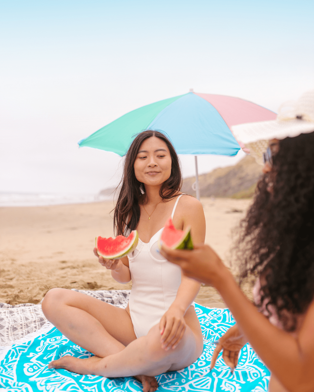 Young Asian woman eating watermelon on the beach representing people wearing acne safe sunscreen.