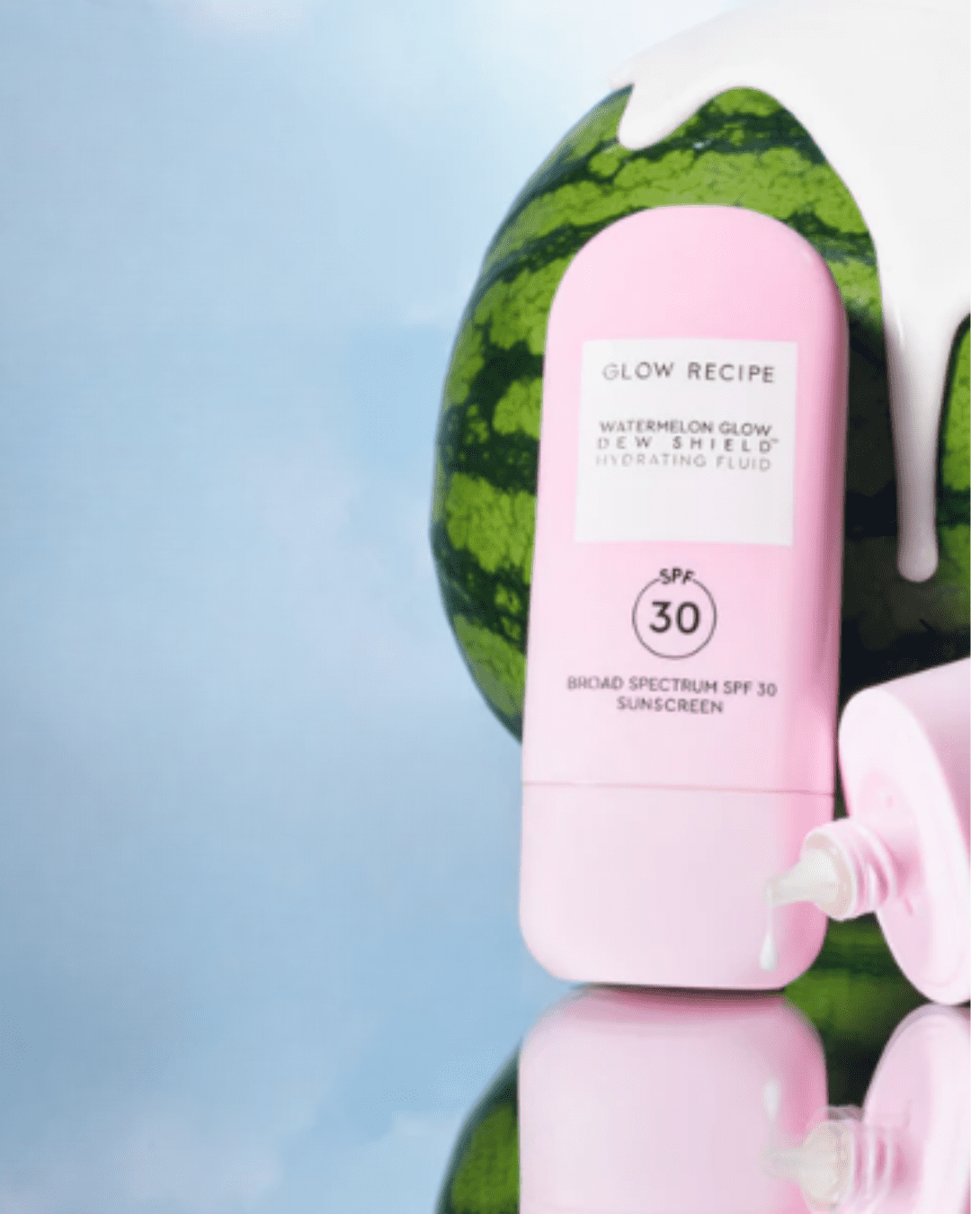 Glow Recipe Watermelon Glow Dew Shield SPF 30 on a mirrored surface showing its reflection, sunscreen coming out of the top, leaning against watermelon, suitable for acne.