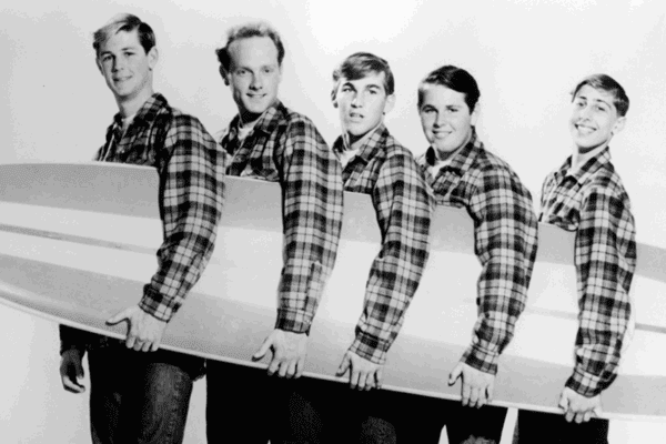 The Beach Boys holding a surfboard in black-and-white-iconic inspiration for beach perfumes.