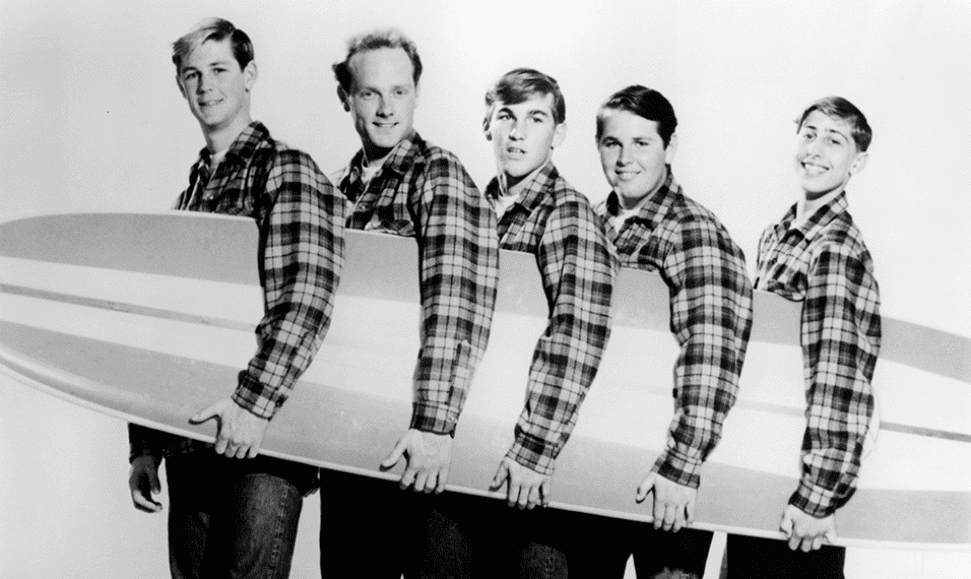 The Beach Boys holding a surfboard in black-and-white-iconic inspiration for beach perfumes.