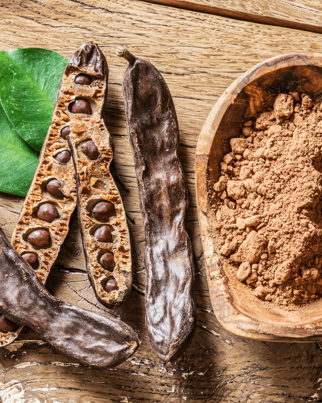 Carob Seeds and ground carob powder on wooden surface, nourishing botanical used in To Go Spa Third Eye Mask.
