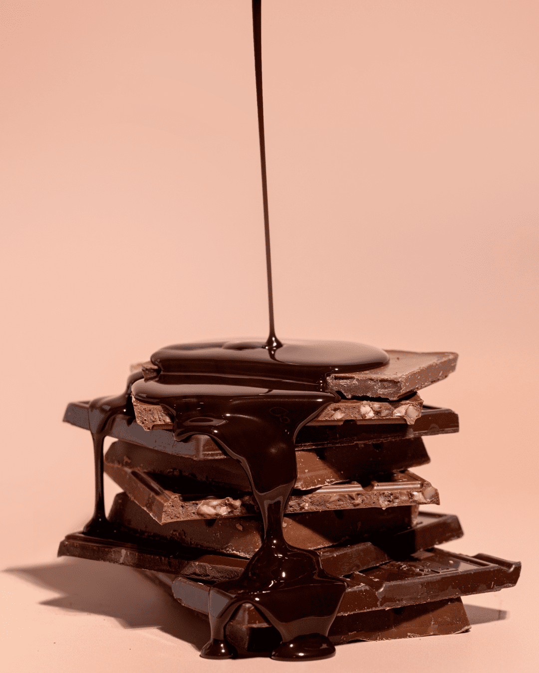 squares of chocolate stacked on top of each other with melted chocolate being poured on top of them