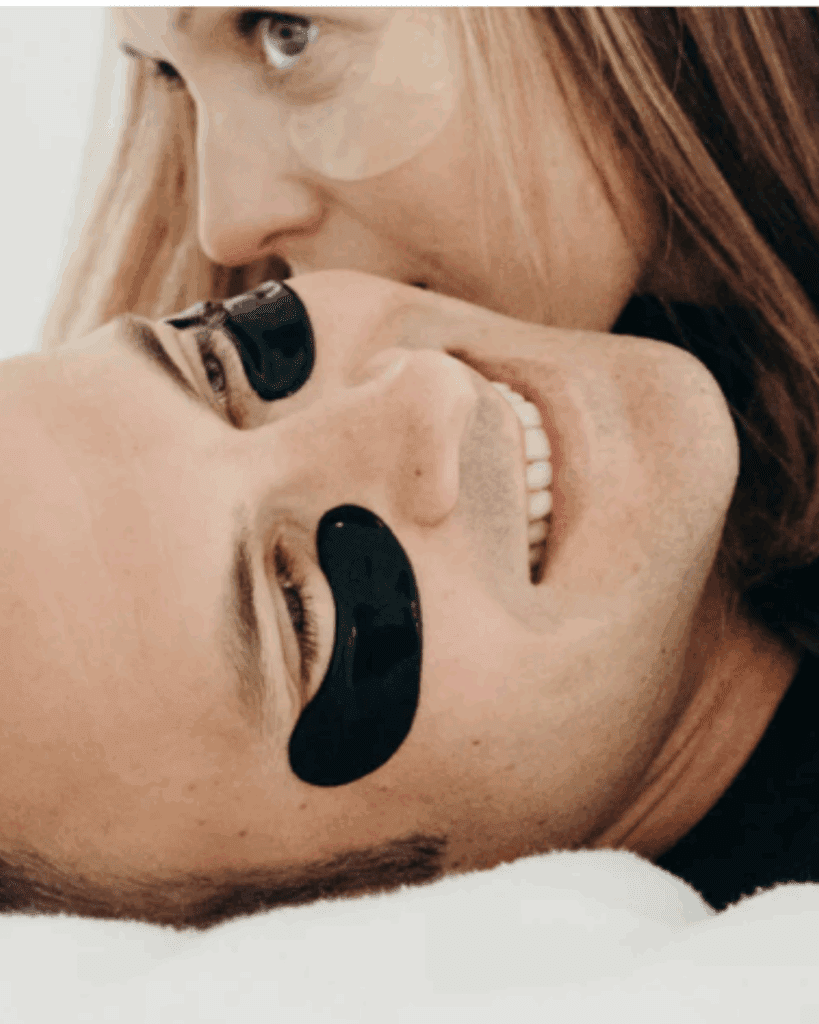 White couple lying on a bed; the husband is wearing To Go Spa Black Bamboo Charcoal Under Eye Patches while resting.
