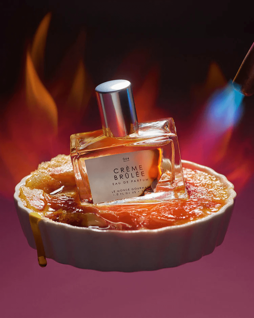Le Monde Gourmand Crème Brûlée Eau de Parfum bottle styled inside a white ceramic dish with Crème Brûlée and torch flames in the background, evoking gourmand sweetness.