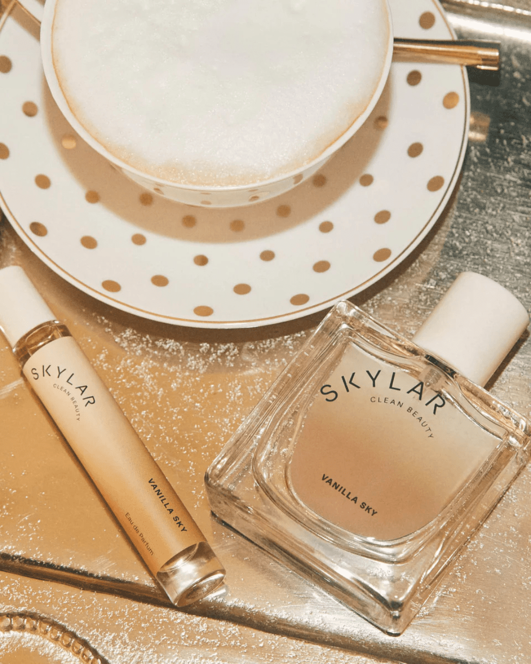 Vanilla Sky Perfume by Skylar Clean Beauty with travel size bottle next to a coffee cup on a display table, emphasizing this comforting and creamy ice cream perfume.