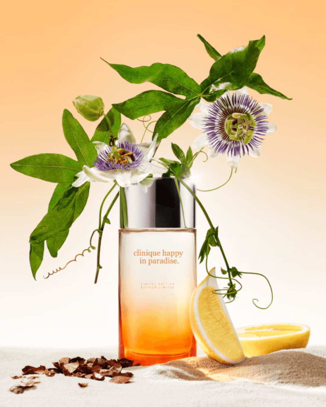 Clinique Happy in Paradise perfume bottle on sand with lemon wedge, white passionflower, and cocoa shells-fresh citrus beach perfumes.