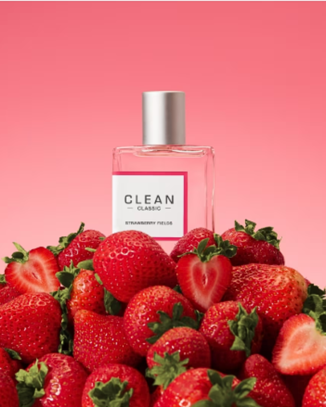 Clean Classic Strawberry Fields Eau de Parfum bottle resting on a pile of strawberries with a soft pink-to-dark pink gradient background, representing strawberry perfumes.