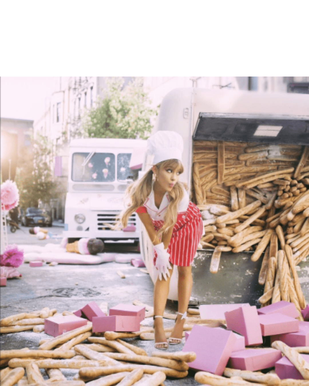 Ariana Grande in a chef hat and white gloves surrounded by donuts, French rolls, and ice cream cones. Scene from Sweet Like Candy Eau de Parfum video emphasizes whimsical candy perfume vibes.