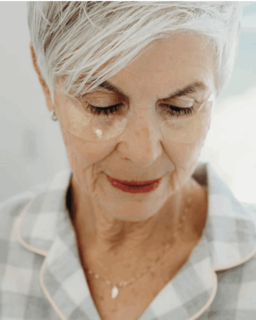 Older white woman wearing a gray and white checkered shirt, wearing To Go Spa Gold Under Eye Patches under her eyes.