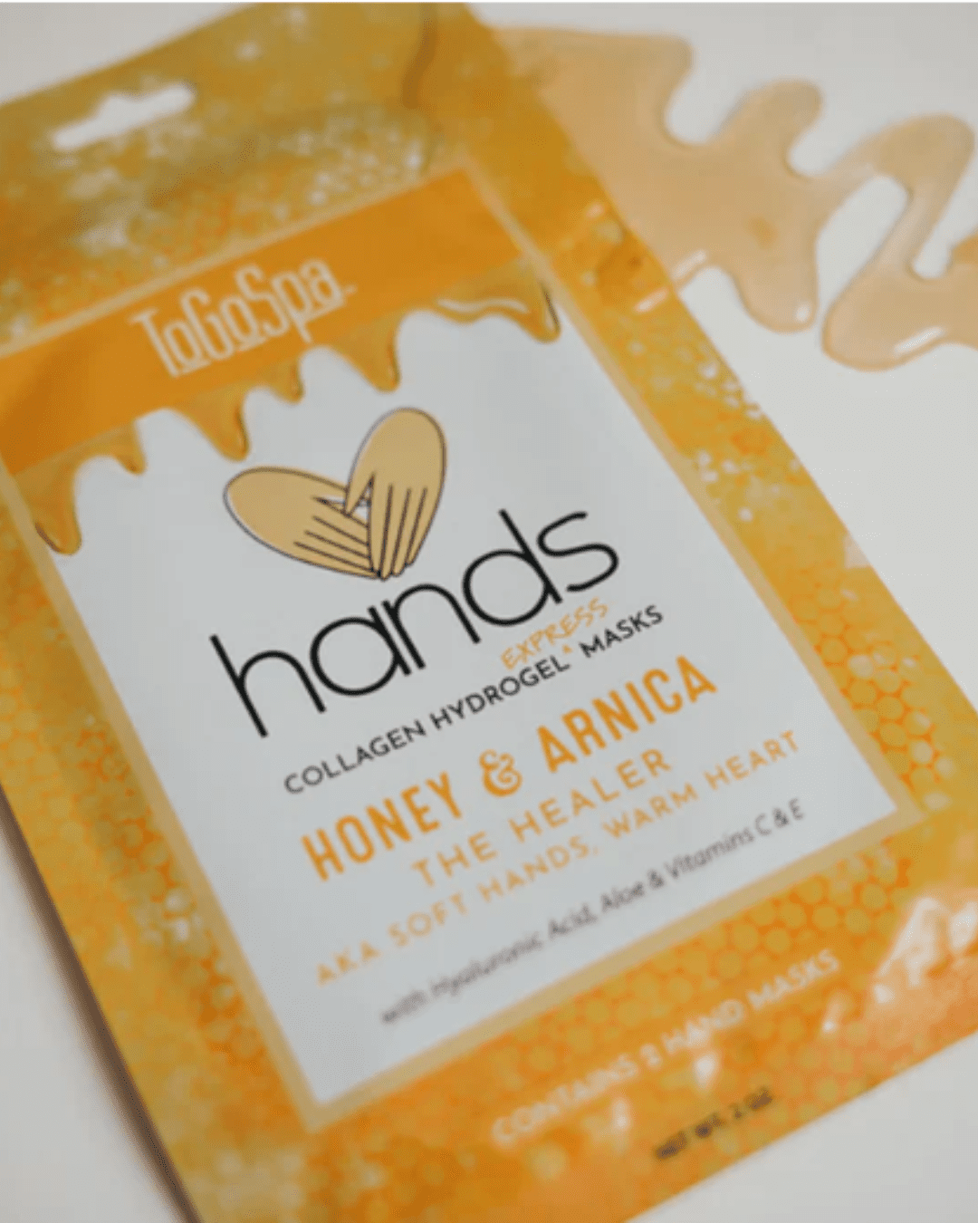 To Go Spa Honey + Arnica HANDS package lying flat with visible serum along the back of the product.