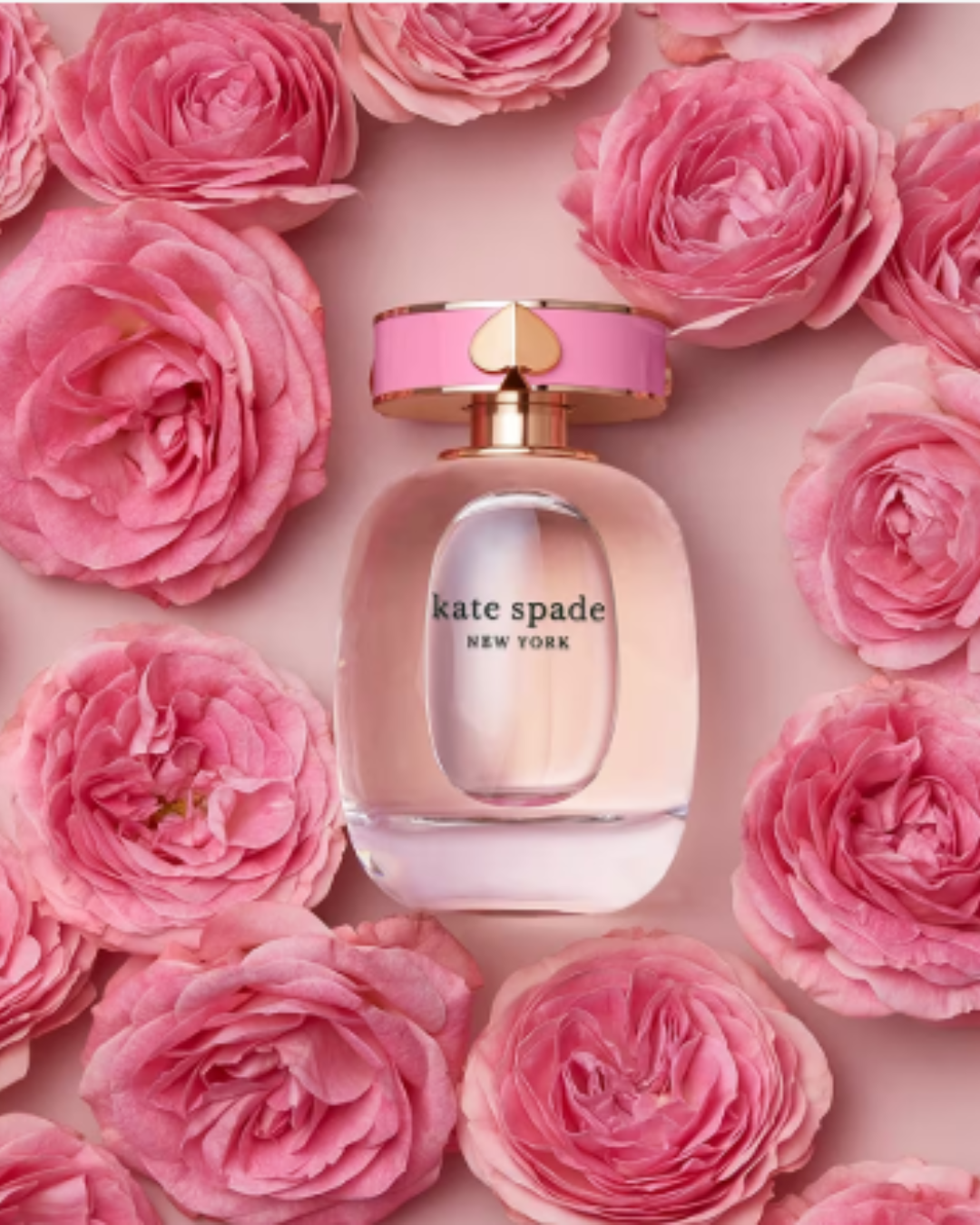 Kate Spade New York Eau de Parfum bottle displayed on a muted pink backdrop surrounded by delicate pink roses, highlighting this strawberry perfume in the strawberry perfumes collection.