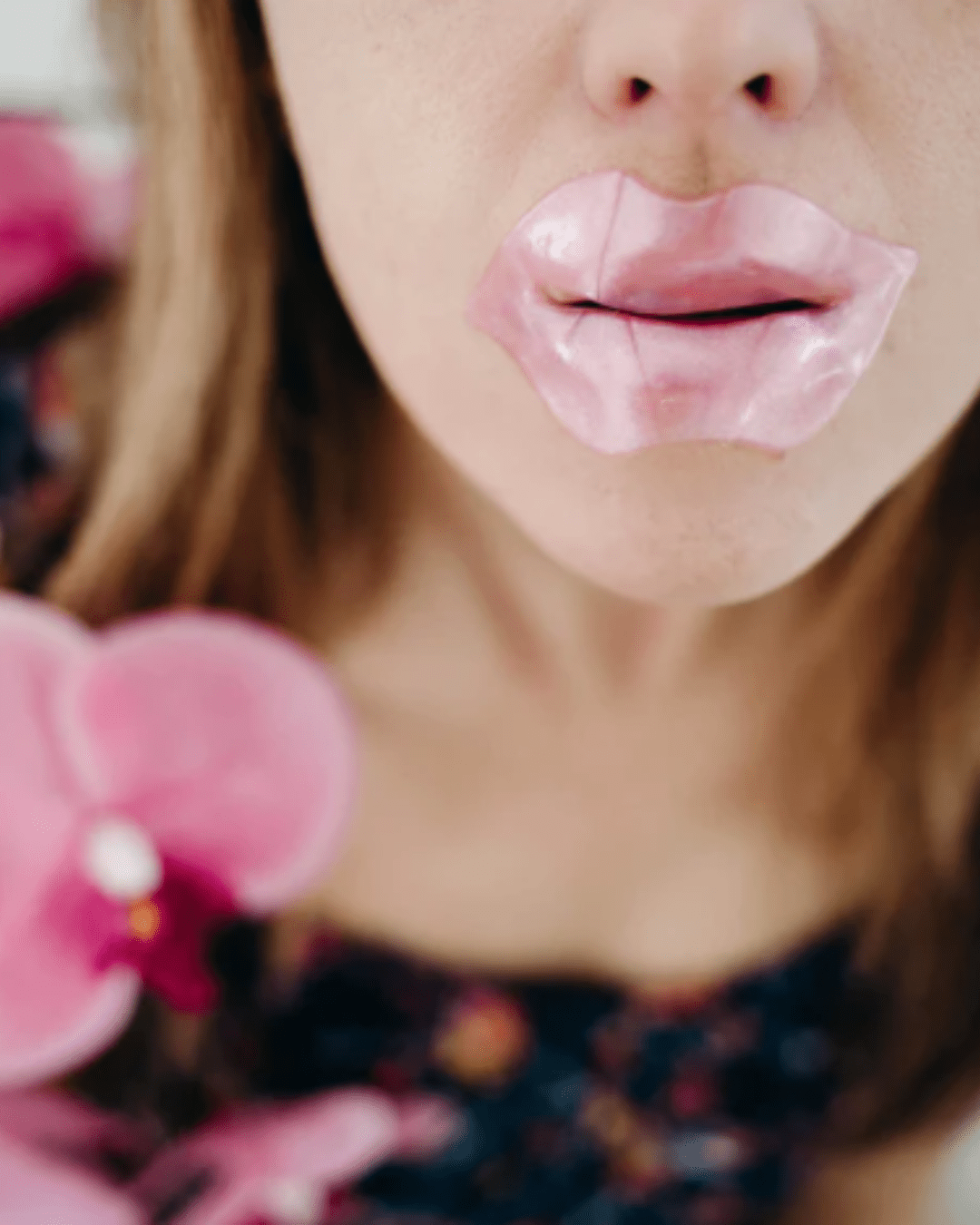 Woman wearing To Go Spa Rose Gold LIPS The Perfect Pucker mask, holding pink orchids in a beauty shot.