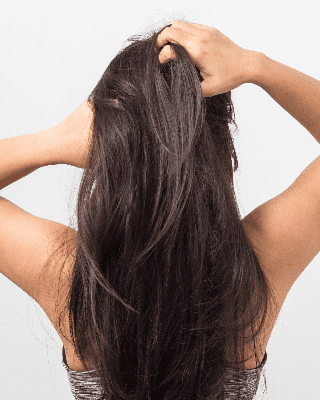 Brown-skinned woman with long dark brown hair running her hands through her hair, showing natural texture and movement, separating her hair to apply Carpe Scalp Serum for Oil and Sweat Control.