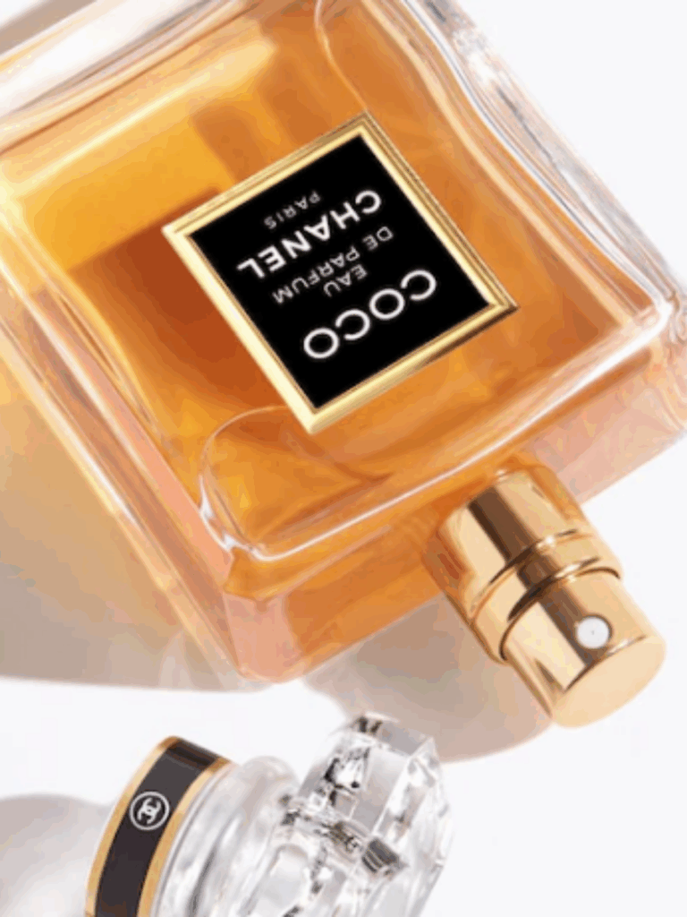 Upside-down Coco Chanel perfume bottle on a white surface with the cap removed, giving a close-up view of the amber-gold perfume inside.