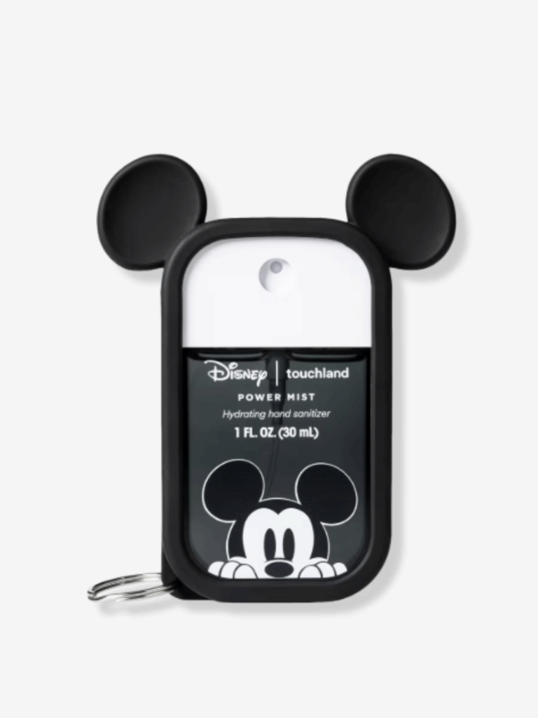 Touchland x Disney Mickey Mouse Power Mist Hand Sanitizer displayed on an off-white surface with a clean, white background. The sanitizer features a sleek black case with signature Mickey Mouse ears and a keychain attachment for bags or keys.