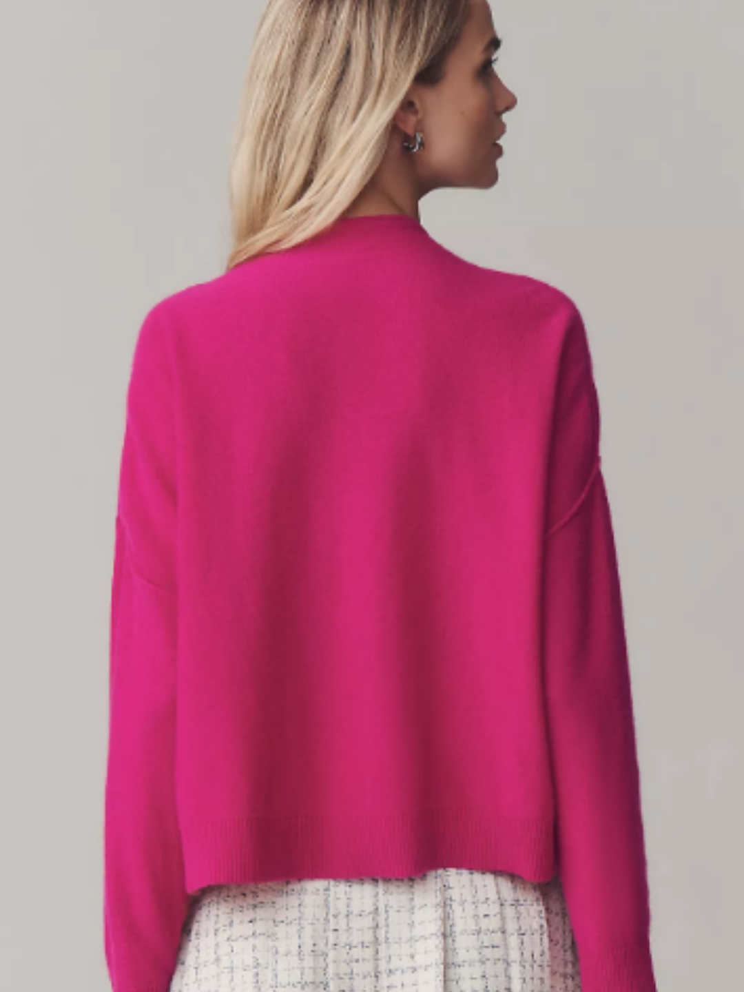 Back view of a woman wearing a pink cashmere mock-neck sweater by Pilcro, highlighting the fit and texture of the knit against a muted gray-brown backdrop.