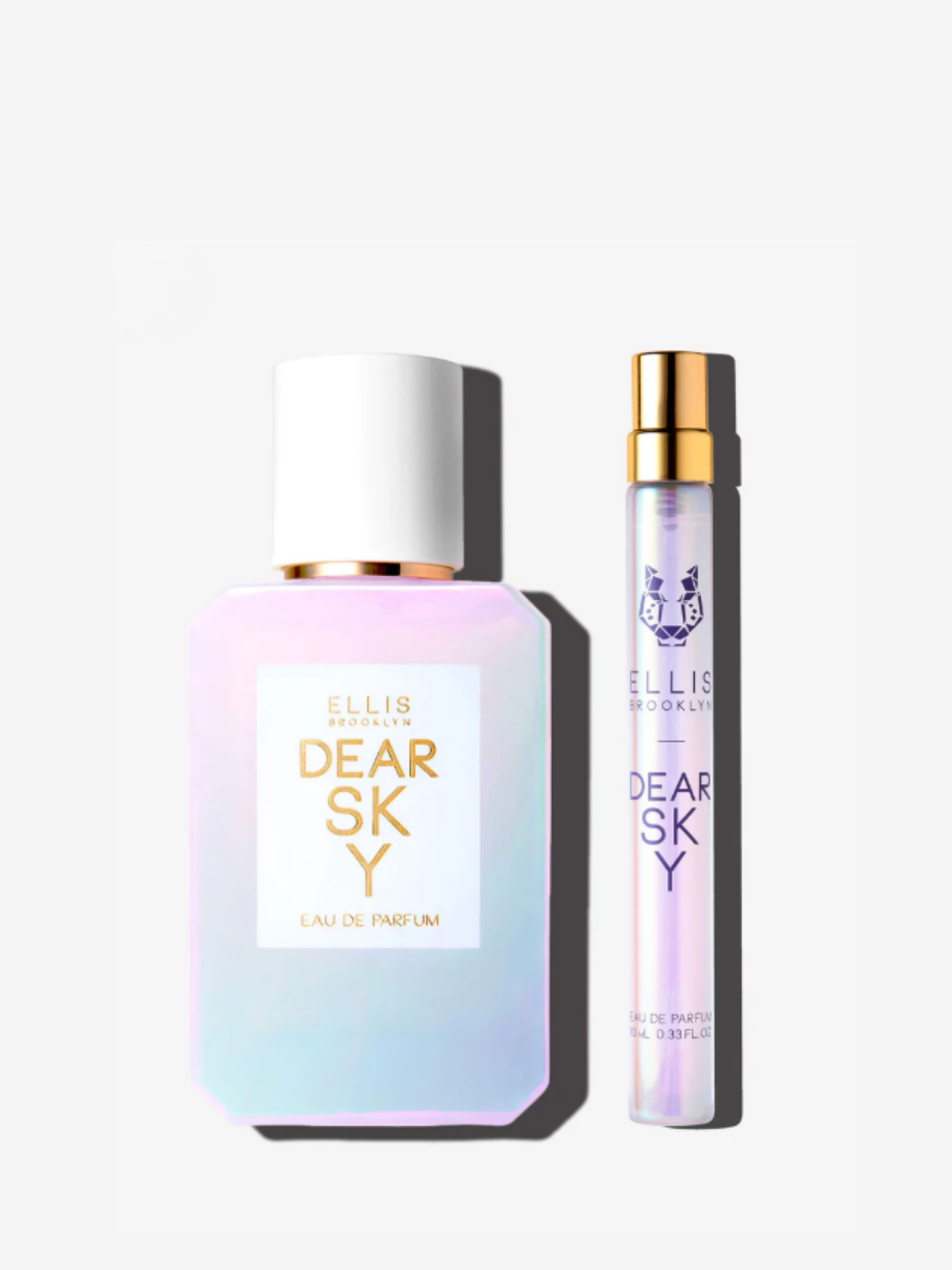Flat lay of the full-size and travel-size Ellis Brooklyn Dear Sky perfume on an off-white background with soft shadows. The minimalist setup emphasizes the scent's bright strawberry note and its clean, sunlit interpretation of the American West.
