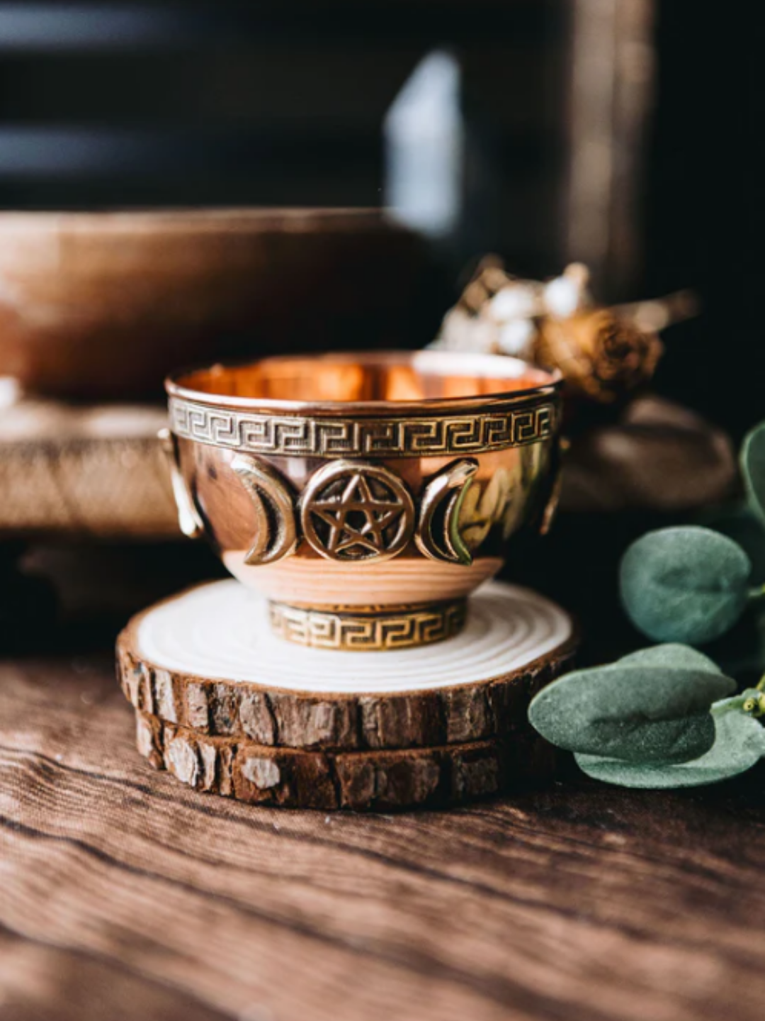 Copper-toned Triple Moon offering bowl from Tamed Wild resting on two small wooden discs on a wooden table, a with soft greenery blurred in the background. The warm tones and natural textures create a strawberry-season atmosphere that aligns with Strawberry Moon rituals.